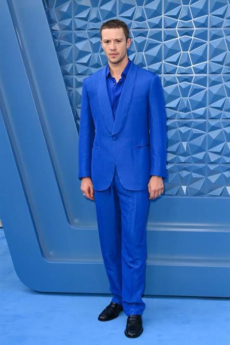 Joseph Quinn standing in flat sandals at a public event